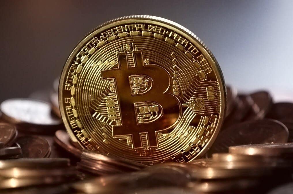 A gold coin emblazoned with the bitcoin symbol resting on a collection of various other coins.
