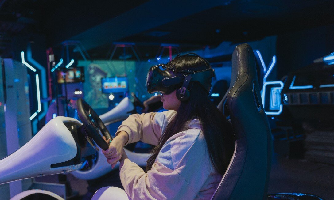 A young girl is seen wearing virtual reality goggles while engaged in a driving simulator.
